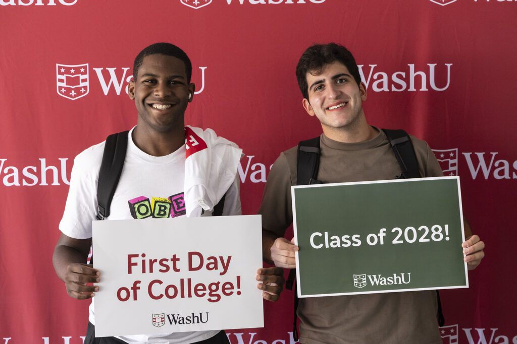 Two students with first day photos with a red backdrop behind them